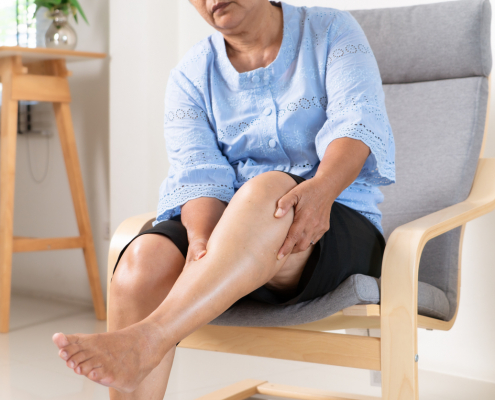 An older woman holding her leg in the air as she looks it while contemplating whether or not she should undergoing the sclerotherapy procedure.